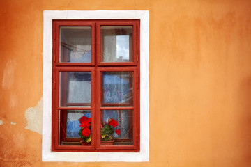 Fototapeta na wymiar An old window with red flowers in orange wall, copy space on the side.