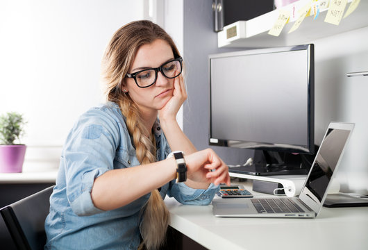 Tired woman at home office looking at watch