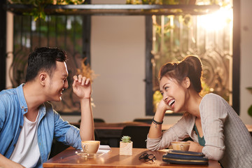 Side view portrait of laughing Asian couple enjoying date in cafe - obrazy, fototapety, plakaty