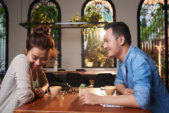 Side view portrait of loving Asian couple meeting in cafe for date, chatting and flirting affectionately