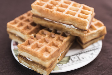 Delicious Viennese waffles with a filling lie on a saucer on a dark brown background, close-up