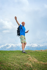 Joyful traveler is standing in the mountains with tablet computer