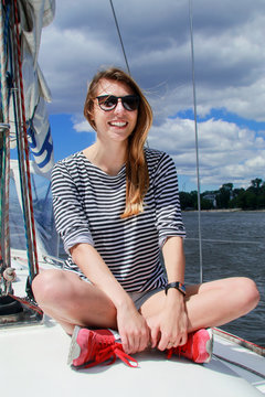 Pretty woman sits on a yacht and smiles, against the blue sky