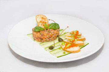 Salmon tartare on a white plate with green leaves