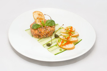 Salmon tartare on a white plate with green leaves