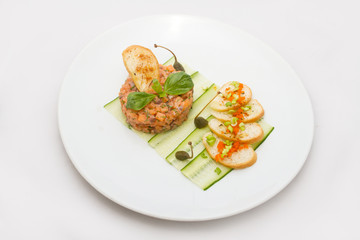 Salmon tartare on a white plate with green leaves
