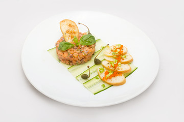 Salmon tartare on a white plate with green leaves