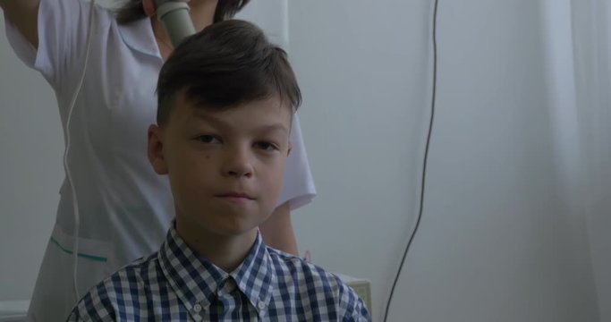 Child uses darsonval for massage head's skin. Receiving electric darsonval facial massage procedure. Receiving electric darsonval body, neck and back massage procedure against pain, Medical Spa