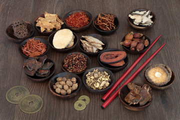 Chinese herbal medicine selection in wooden bowls with feng shui coins and chopsticks on oak background.