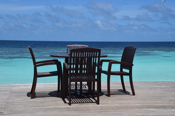 Stühle und Tische auf einem maledivischen Sonnendeck mit schöner türkisfarbener Lagune und blauem Himmel