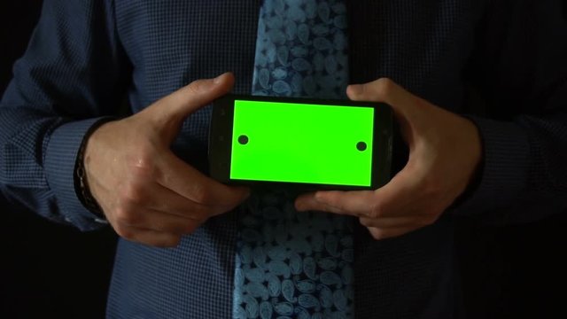Man holds smartphone to camera with green screen.