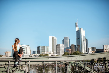 Young woman in sportswear sitting on the bridge after the training with great view on the modern...