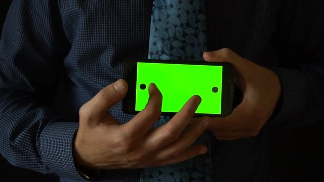 Man holds smartphone to camera with green screen.
