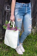 teen girl in frayed blue jeans carrying lilac bouquet in muslin sack