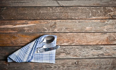 Spoon, fork, knife wrapped in a blue plaid towel. Cutlery lies on an old wooden table. Top view. 