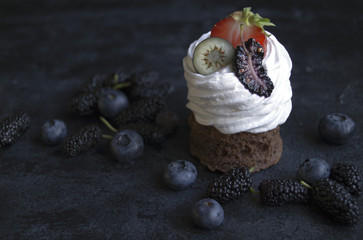 Chocolate cake with berries, blueberry and mulberry. On a black background. A dark photo.