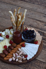 Cheese plates served with grissini, crackers, dates, jam, olives and nuts on wooden background