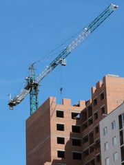 Building crane and building under construction against blue sky.