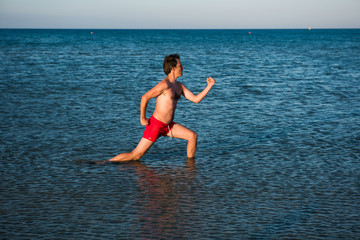 Slim guy posing in red swimwear in sea water