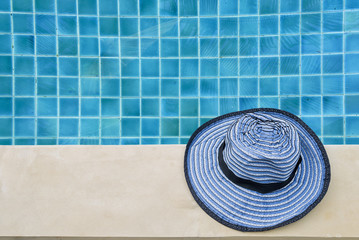 Summer concept, blue design hat over Crystal clear swimming pool water 