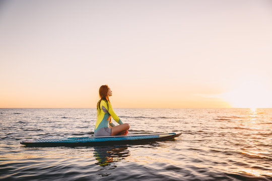 Stand up paddle boarding on a quiet sea with warm sunset colors. Young woman is relaxing on ocean