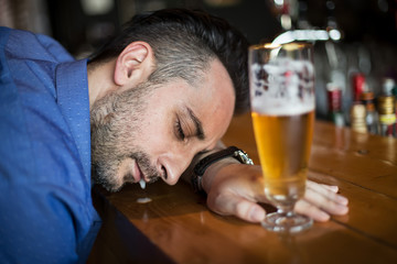A drunk bearded man holding a glass of beer in his hand and sleeping in the bar
