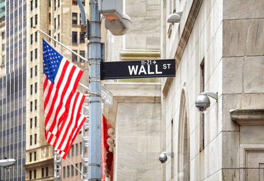 Wall Street sign with American flag in distance, shallow depth of field, New York City, USA