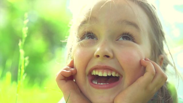 Portrait of a happy smiling little girl lying on green grass. Slow motion 4K UHD video 3840X2160