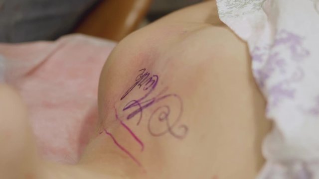 Body of woman breathing hard during tattoo session. Tattoo artist wipes dry skin and strats tattooing. Slow motion view