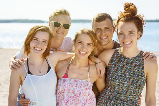 Group of happy students posing arm in arm on a beach