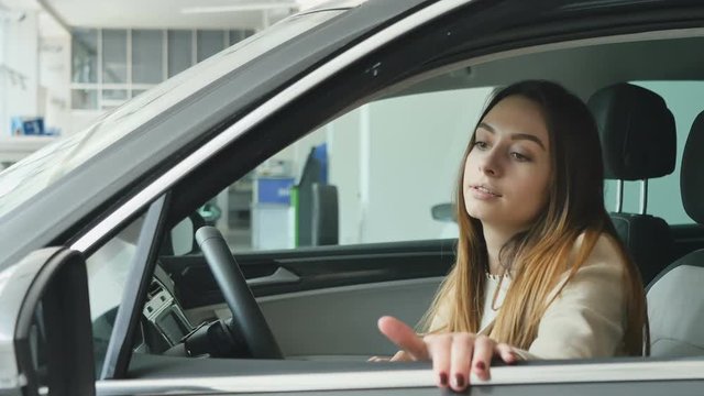 Beautiful woman inspects the cabin of modern car in showroom