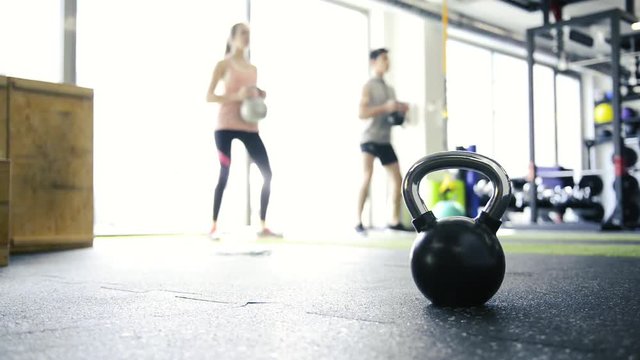 Young fit couple in gym exercising with kettlebell.