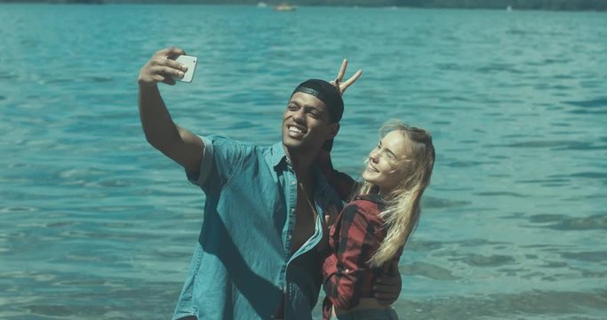 Young adult interracial couple taking a selfie on a beach, Caucasian female and African American man in casual clothes enjoying summer day