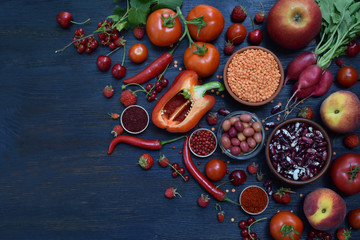 Obraz na płótnie Canvas composition of red vegetarian products: fruits, vegetables, spices and beans on wooden background. Apple tomatoes, currant peppers, raspberries cherry, lentils. Healthy food. Copy space for text