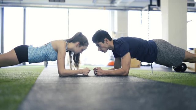Young fit couple in gym in plank position exercising core muscle