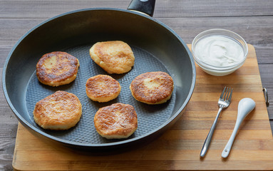 pancakes made from curd cheese on a frying pan with little plate with sour cream and cutlery