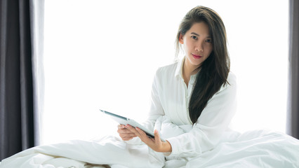 Asian woman use a tablet on the bed after wake up in weekend mornning.Use the tablet to read news, watch movies, or chat in relex and Communications, social media concept.