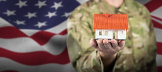 Composite image of mid section of soldier holding model house