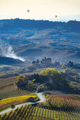 Road between the hills of Langa Piemonte Italy, at the bottom the castle of Grinzane cavour, in the sky two balloons