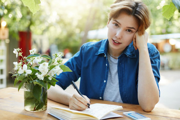 Woman writing in diary. Portrait of a girl taking notes in her notepad outdoors planning a trip or vacation or future business looking at camera wearing velvet blue shirt in park.