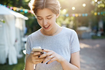 Girl using smart phone. Portrait of a young hipster female using a modern smart phone outdoors texting or scrolling through social media or having a conversation with a boyfriend.