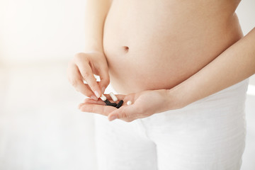 Closeup of pregnant soon to be mother holding pills and medications or vitamins. Healthy motherhood concept. High key.