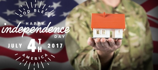 Composite image of mid section of soldier holding model house