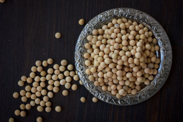 Soybeans in metal plate over black wooden background.