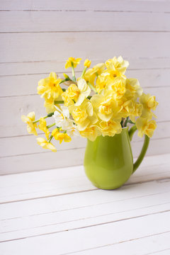 Bright yellow spring daffodils or narcissus flowers in pitcher on white  wooden background.