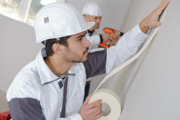 worker protecting batten moulding with masking tape before painting