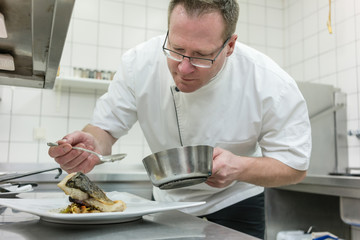 Koch beim Anrichten und Garnieren von Fischgericht auf dem Pass in der Restaurant Küche