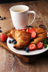 Delicious breakfast with fresh croissants, coffee and ripe berries on old wooden background