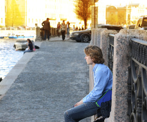 A teenager sitting near a river on a city street