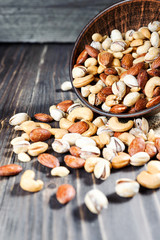 Mixed nuts spilling out of bowl on wooden table. Macro still-life with shallow dof